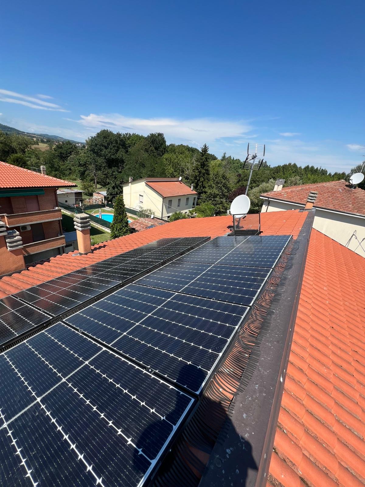 Pannelli fotovoltaici installati su tetto di tegole rosse di una casa residenziale con montagne e alberi circostanti