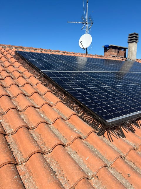 Solar panels and satellite dish installed on a terracotta tiled roof against a clear blue sky