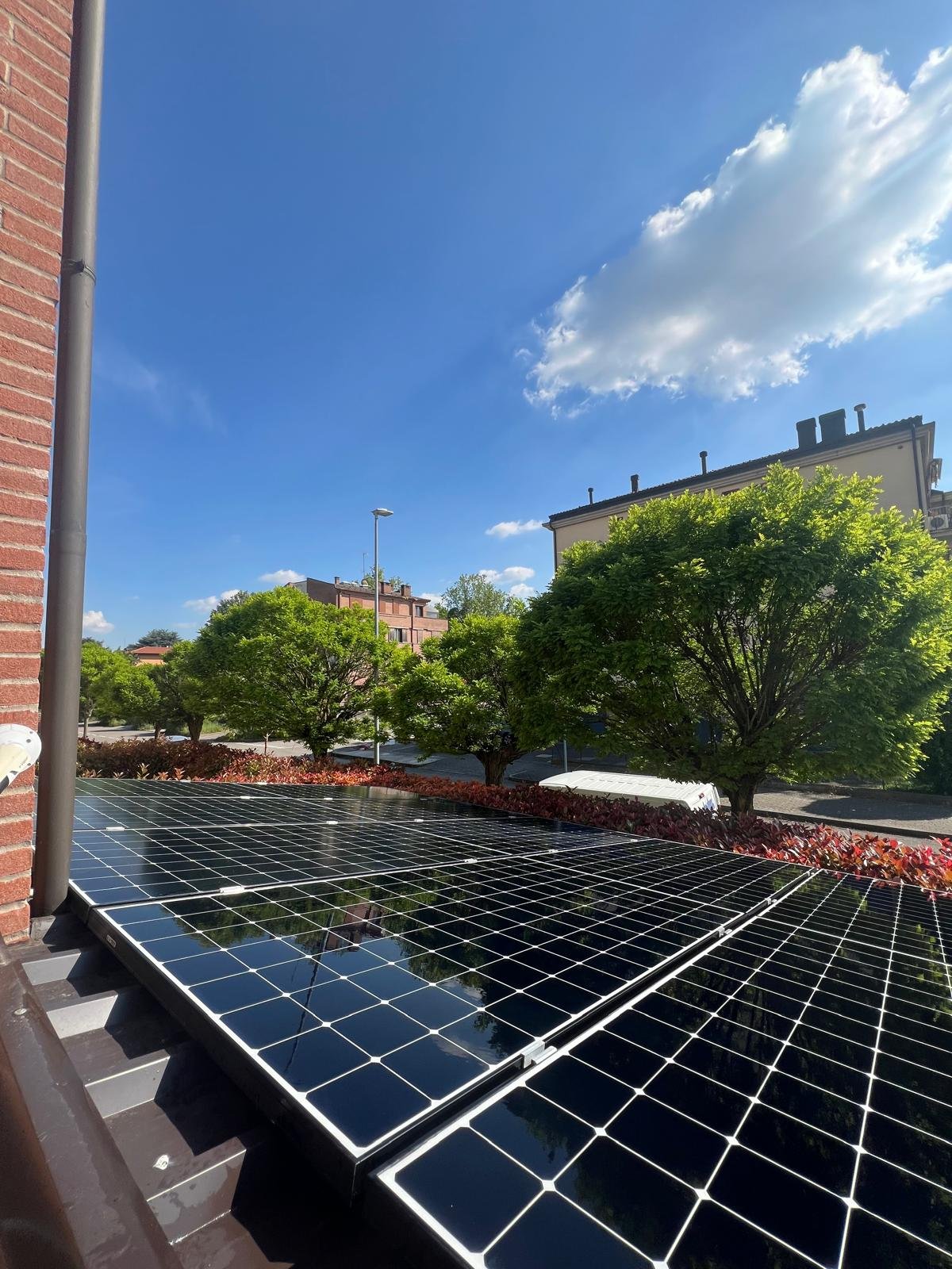 Pannelli solari installati su tetto di edificio urbano con alberi e cielo blu con nuvole